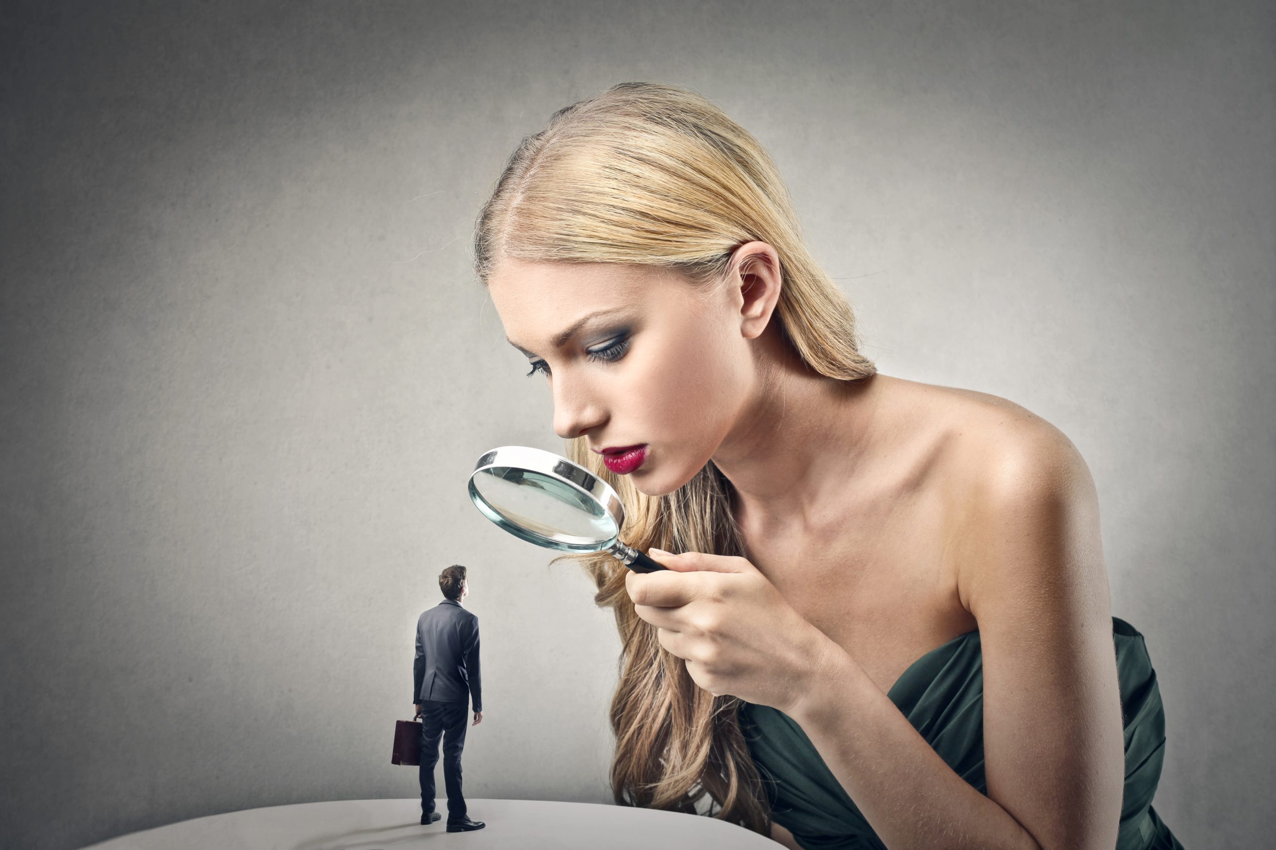 a giantess story a tall blonde woman looking at a tiny man with a magnifying glass