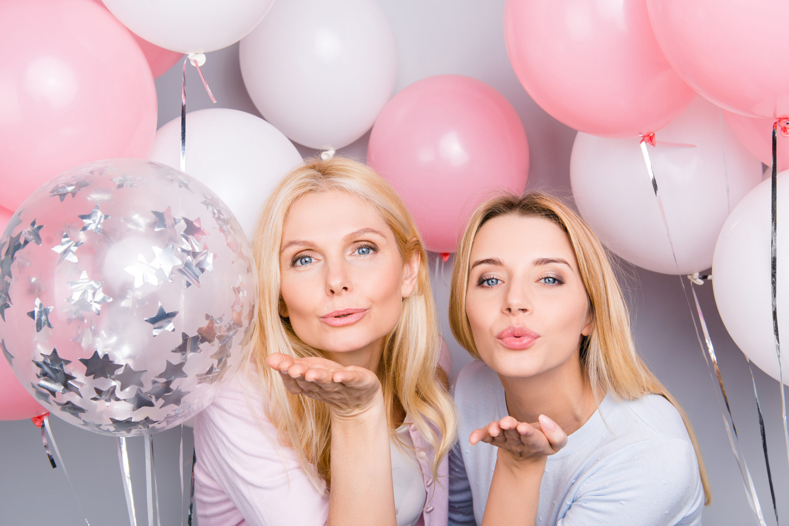 girls trip step mother and step daughter blowing kisses in front of pink balloons on a girls trip